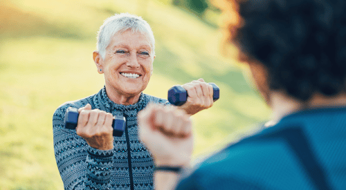 A grey-haired woman lifts light weights as part of an exercise program